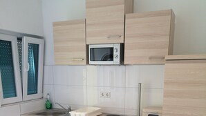 Ett modernt kök med ljusa träskåp, en mikrovågsugn, en diskmaskin från Bosch och ett fönster med persienner.