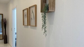 Um corredor com prateleira de madeira, duas fotos emolduradas e uma planta pendurada.