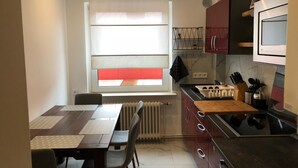 Uma cozinha compacta com área de refeições, uma janela com persianas, micro-ondas embutido e uma pia pequena.