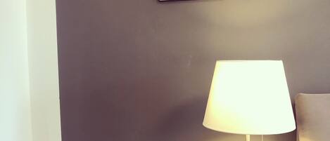 A room with a dark wall, a small table with a lamp, and two framed mirrors.