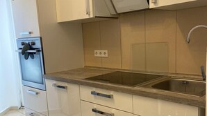 Uma cozinha moderna com armários brancos, forno embutido, pia de aço inoxidável e micro-ondas.