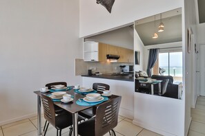 Uma sala de jantar moderna com uma mesa posta para quatro pessoas, cozinha ao fundo e varanda com vista.