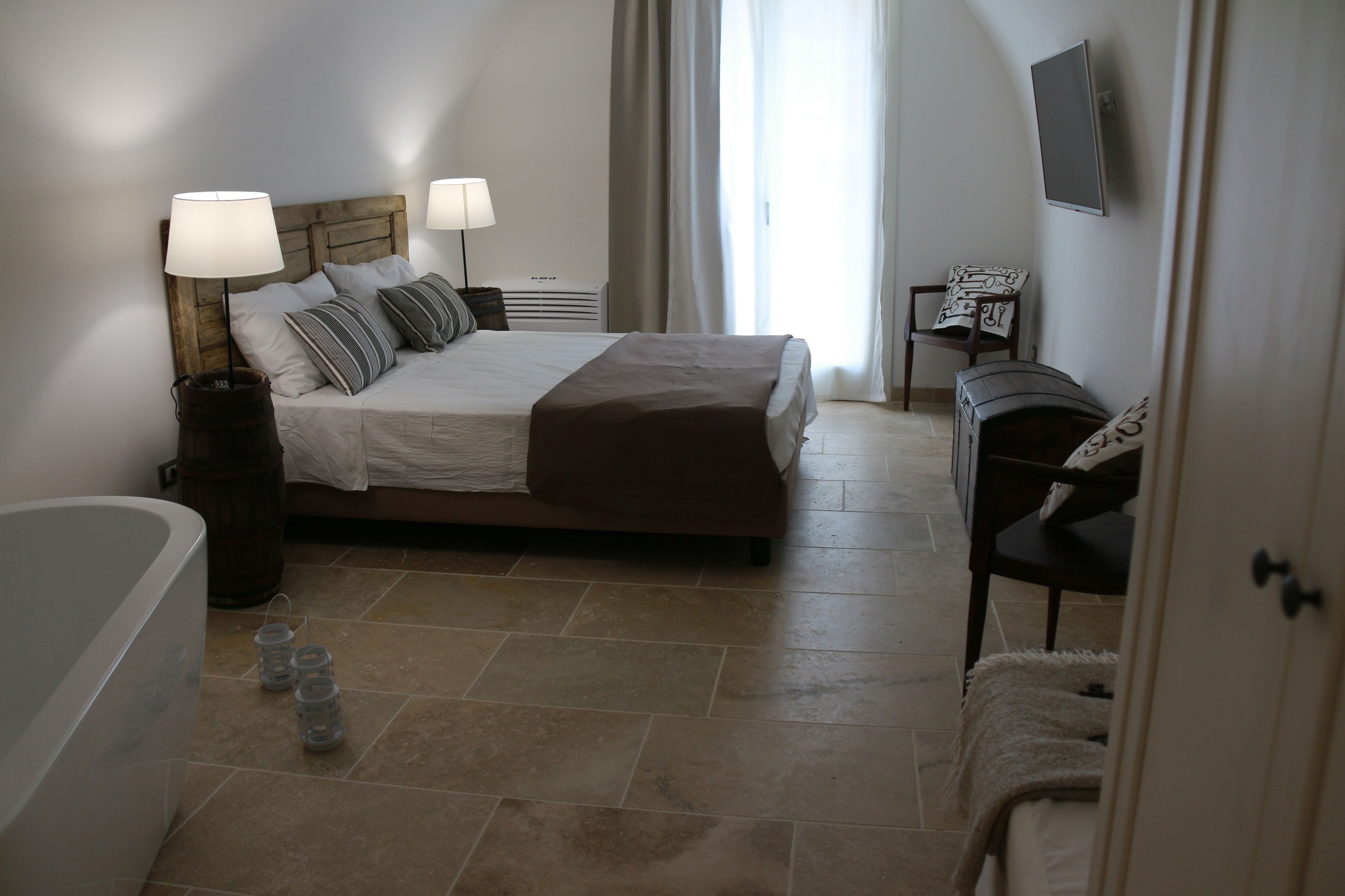 A bedroom with a bed, bedside lamps, a TV on the wall, a chair, and a small table.