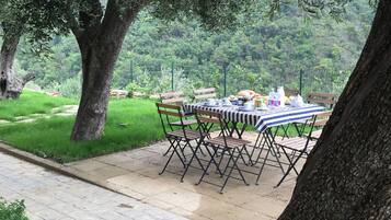 Un área de comedor al aire libre con una mesa preparada para cuatro personas, rodeada de árboles y un paisaje cubierto de césped.