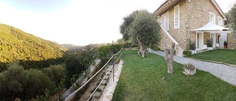 Un edificio de piedra con un camino empedrado, un pequeño jardín y vistas a una colina.