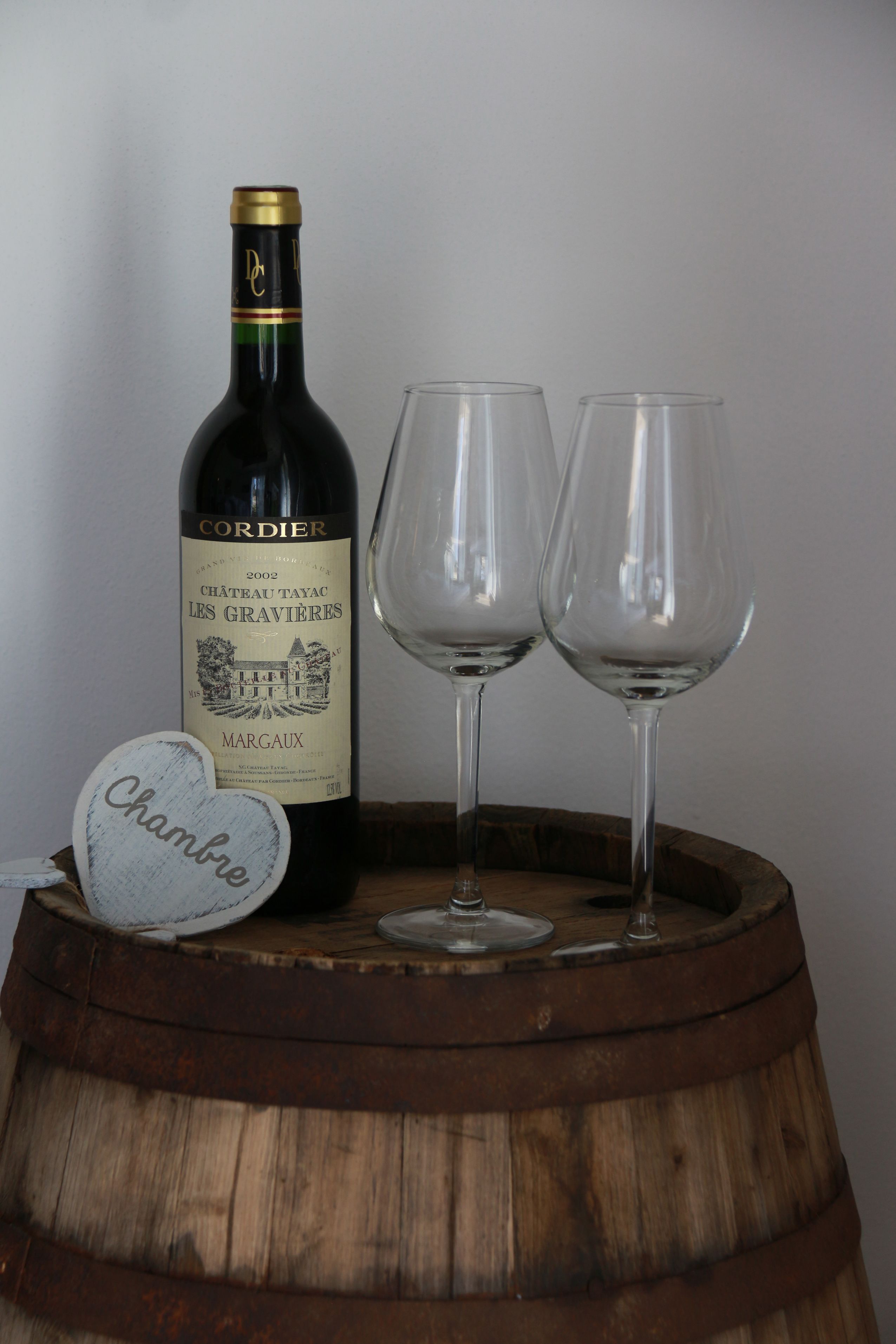A bottle of wine, two empty wine glasses, and a wooden barrel.