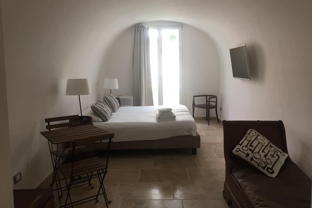 Un dormitorio con cama, mesitas de noche, escritorio, silla, televisor y ventana con cortinas.