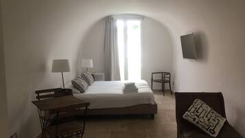 Ein Schlafzimmer mit Bett, Nachttischen, Schreibtisch, Stuhl, Fernseher und einem Fenster mit Vorhängen.