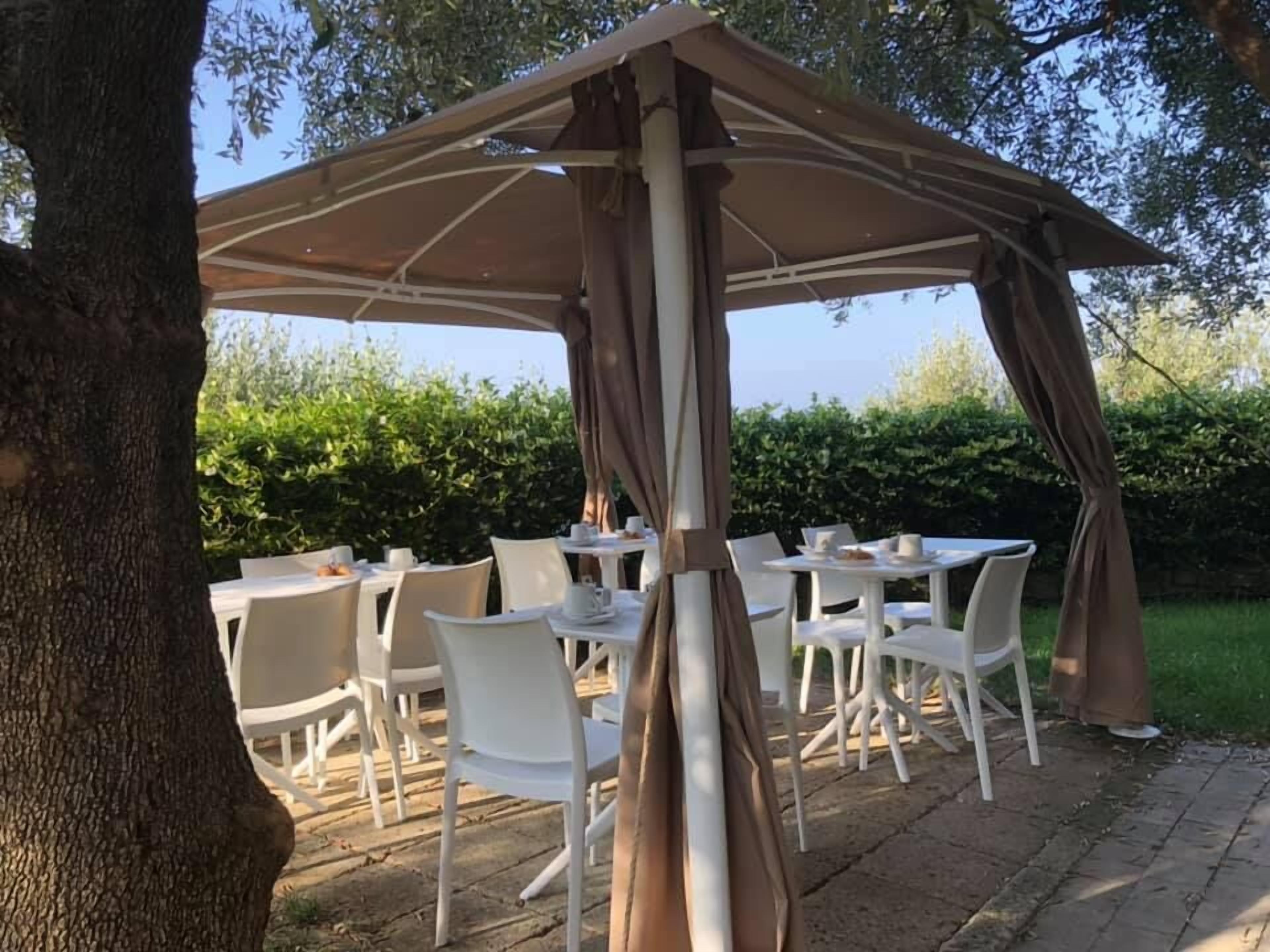 Une terrasse extérieure avec des tables et des chaises blanches, protégée par un grand parasol.