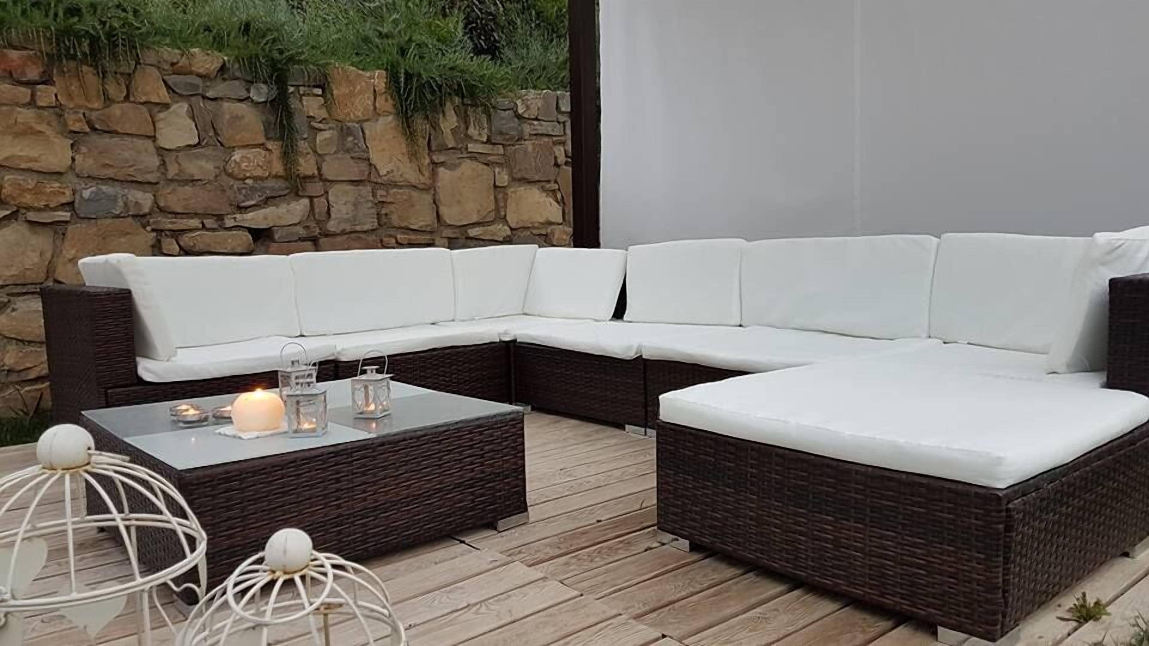 A sectional sofa with white cushions, a glass coffee table with candles, and wicker furniture.