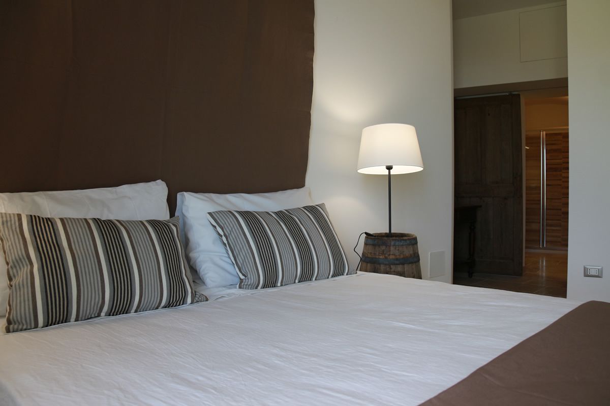 A bedroom with a large bed, two striped pillows, a bedside lamp, and a wooden barrel.