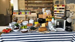 Een ontbijtbuffet met diverse etenswaren en dranken, waaronder fruit, gebak en toevoegingen, met een rustieke stenen muur op de achtergrond.