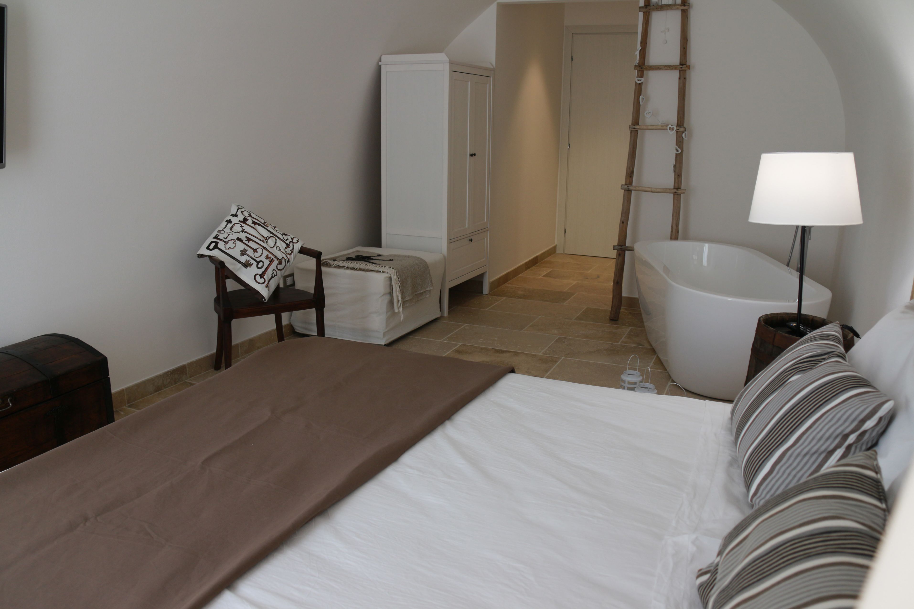 Un dormitorio con cama, una silla, armario, bañera y lámpara de noche.