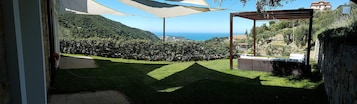 Un patio con vista al mar, una pérgola y un muro de piedra.