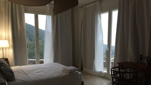 Een hotelkamer met een bed, een tafel en stoelen. Gordijnen en uitzicht op het buiten.