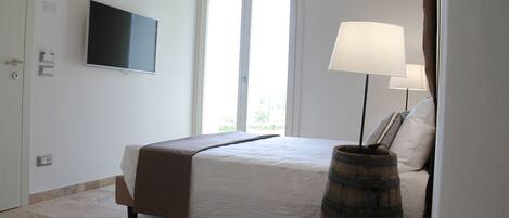 A bedroom with a bed, a television mounted on the wall, a window with a view, and a lamp.