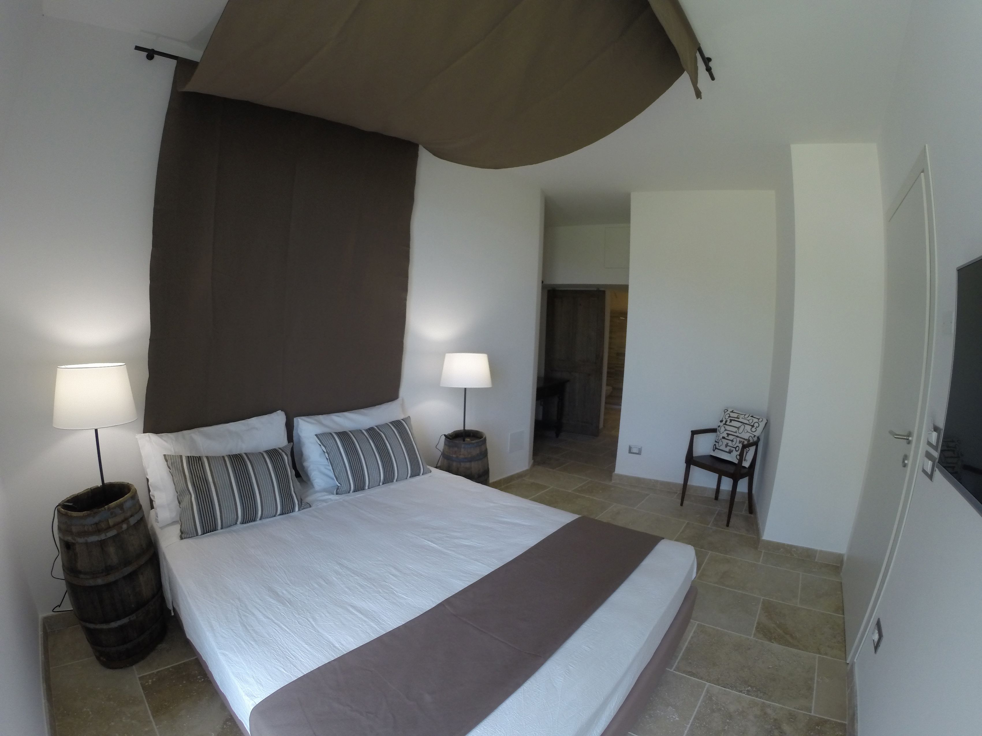 Une chambre à coucher avec un grand lit, deux tables de chevet avec des lampes, une chaise et un téléviseur fixé au mur.