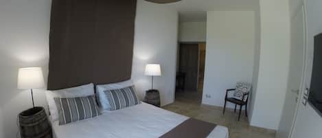 Une chambre à coucher avec un grand lit, deux tables de chevet avec des lampes, une chaise et un téléviseur fixé au mur.