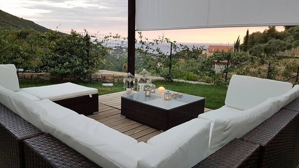 Een terras met rieten meubilair en een tafel met glazen blad, met uitzicht op een schilderachtige omgeving.
