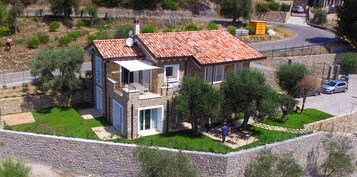 A stone house with a tiled roof, a balcony, and a paved driveway.