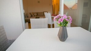 A dining area with a white table, a vase with pink flowers, and a view of a living room with a sofa and chairs. - Apartments Orange (Novalja)