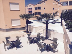 A rooftop patio with outdoor seating and palm trees. - Apartments Orange (Novalja)