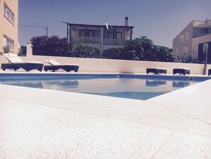 A swimming pool with lounge chairs and a building in the background. - Apartments Orange (Novalja)