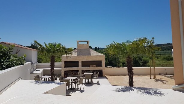 A rooftop terrace with outdoor seating, a barbecue area, and a view of the surrounding landscape. - Apartments Orange (Novalja)