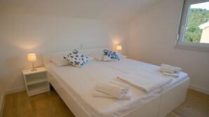 A clean, modern bedroom with a large bed, two bedside tables, and a window with a view of greenery. - Apartments Orange (Novalja)