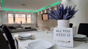 Ein Essbereich mit einem Tisch für vier Personen, einem Schild mit der Aufschrift 'ALL YOU NEED IS' und einer Zierpflanze.