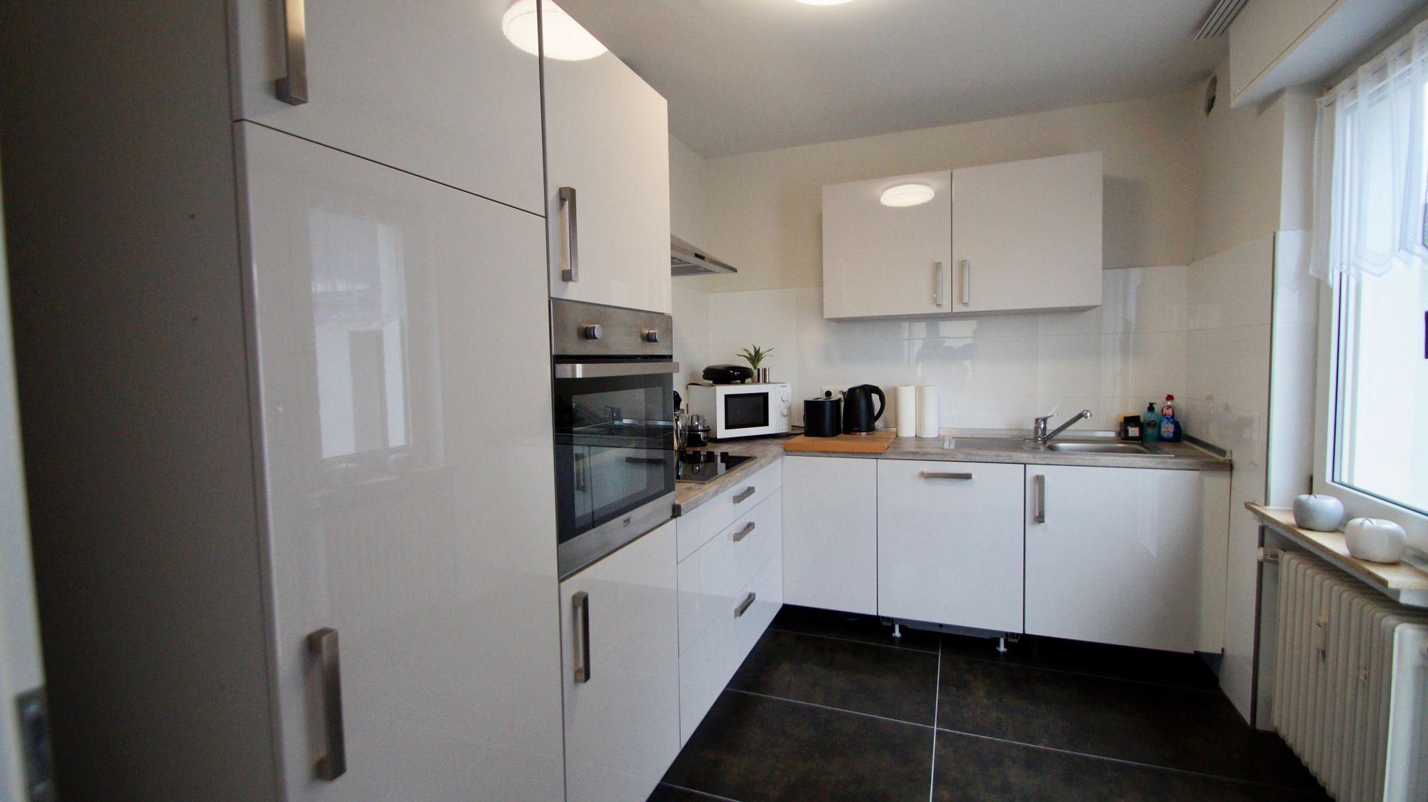 A compact kitchen with white cabinets, a built-in oven, a microwave, and a sink.