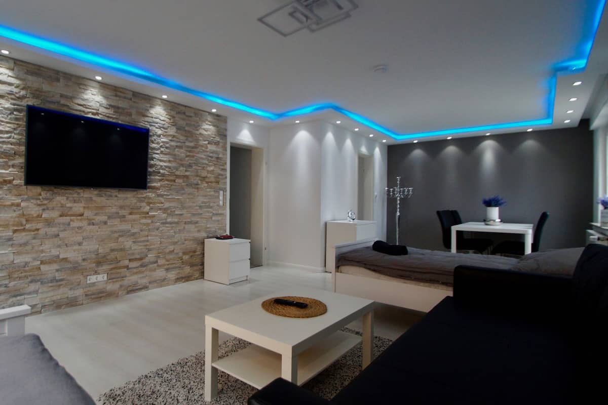 Una sala de estar moderna con una pared de piedra, un televisor de pantalla plana, una mesa de centro blanca y un sofá.