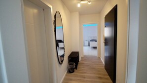 Ein schmales Gang mit einer Bank, einem Mülleimer und einer Tür zu einem Schlafzimmer.