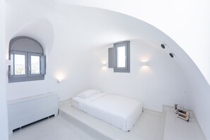 A minimalist white room with a bed, a radiator, and two windows. - Philosophia Luxury Villa (Santorini)