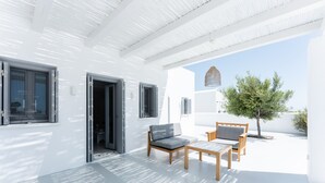 Un bâtiment moderne de couleur blanche, doté d’un patio couvert comprenant une table en bois et deux canapés.
