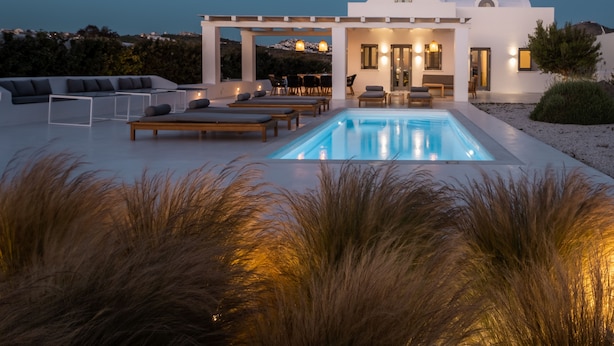 Un espace piscine extérieur moderne, doté de chaises longues et d’une pergola, le tout entouré de hautes herbes.