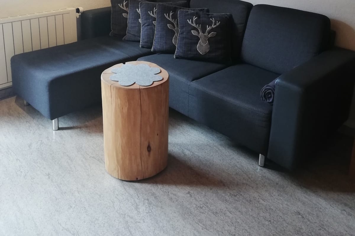 Uma sala de estar moderna com um sofá seccional preto, uma mesa de centro de madeira e uma janela com cortina.