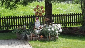 A garden with a wooden fence, a gnome statue, and various plants. - Ferienhaus Pfeifer (Sankt Gallenkirch)