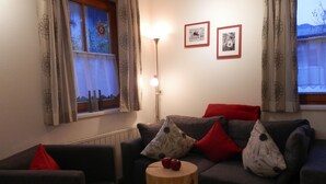 A living room with a grey sofa, red cushions, a wooden side table, and two framed pictures on the wall. - Ferienhaus Pfeifer (Sankt Gallenkirch)