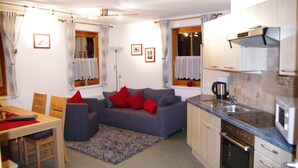 A compact living space with a kitchenette, a dining area, and a sofa with red cushions. - Ferienhaus Pfeifer (Sankt Gallenkirch)