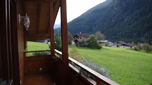 A wooden balcony with a lantern, overlooking a green field and houses in a mountainous area. - Ferienhaus Pfeifer (Sankt Gallenkirch)