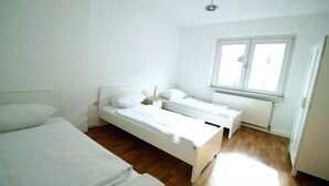Una habitación con dos camas individuales, un ventanal y un radiador.