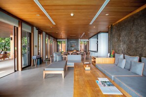 A modern living room with a wooden ceiling, large grey sofa, wooden coffee table, and a television.