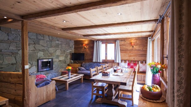 L’intérieur chaleureux d’un chalet avec un mur en pierre, des meubles en bois, un téléviseur et un coin repas.