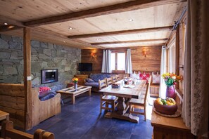 Interior acolhedor de cabana com parede de pedra, móveis de madeira, televisão e área de refeições.