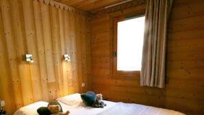 Une chambre dans une cabane en bois, avec un lit, des oreillers, un ours en peluche et une fenêtre avec des rideaux.