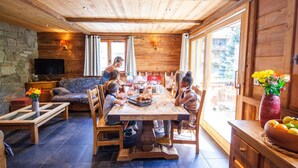 Un intérieur en bois avec un mur en pierre, un téléviseur, une table à manger avec des chaises et un vase rempli de fleurs.