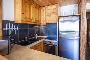 A modern kitchen with wooden cabinets, a stainless steel refrigerator, and a built-in oven. - galta, this warm apartment can accommodate up to 12 people, ideal for large families or stays with friends. (Valloire)
