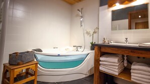 Une salle de bain moderne avec une baignoire sur pieds, un tabouret en bois, un lavabo avec un miroir et une étagère avec des serviettes.