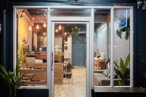 A modern interior with a wooden floor, a seating area with a sofa and chairs, and a counter with a plant. - Private Stay Hostel (Bangkok)